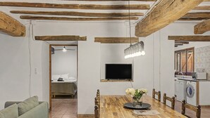 A dining area with a wooden table, chairs, a TV mounted on the wall, and a washing machine in the background.