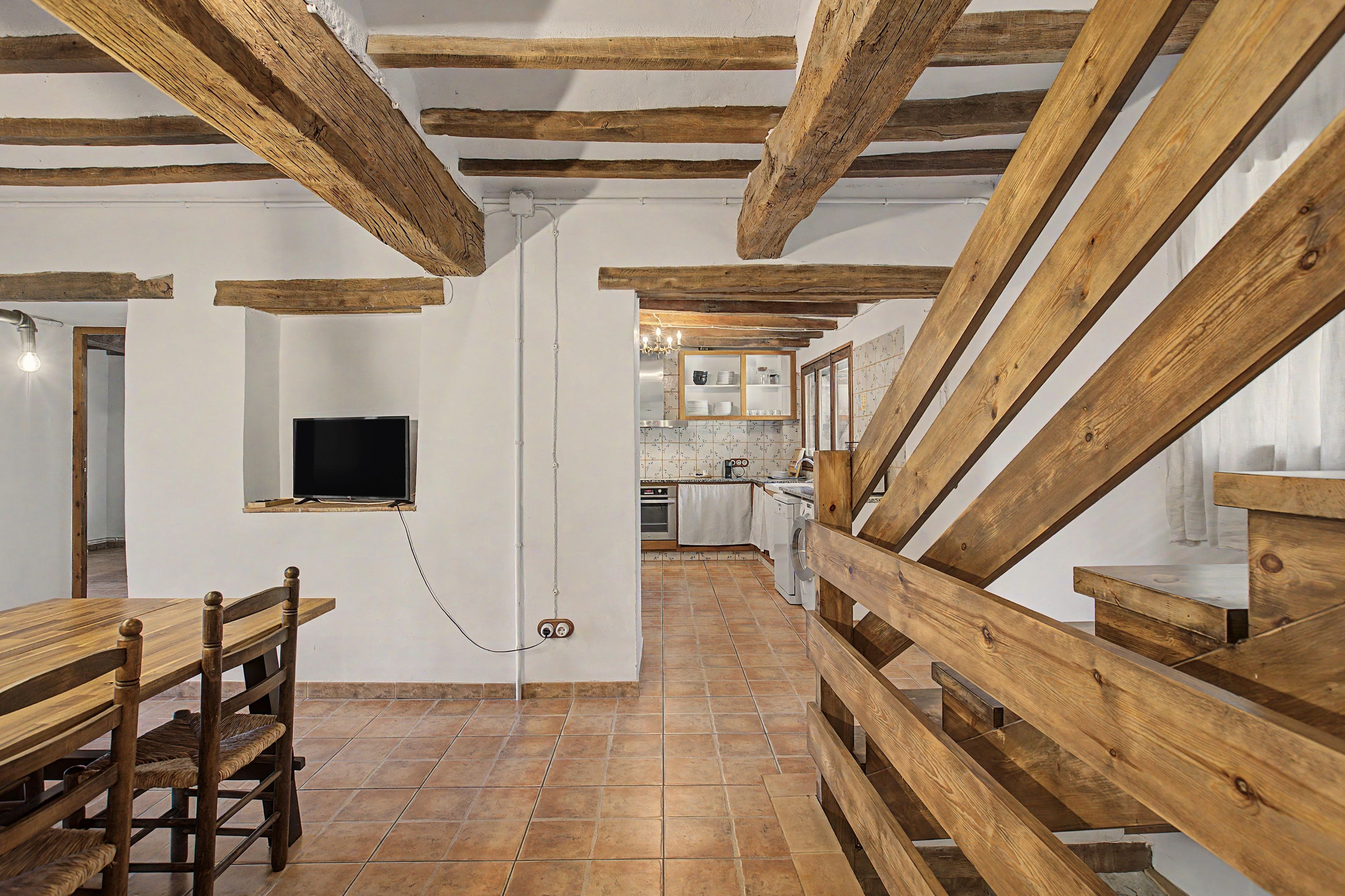Un'atmosfera rustica con travi a vista in legno, pavimento piastrellato, zona pranzo con tavolo e sedie in legno e cucina dotata di elettrodomestici moderni.