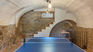 A ping pong table in a room with stone walls and a wooden staircase.
