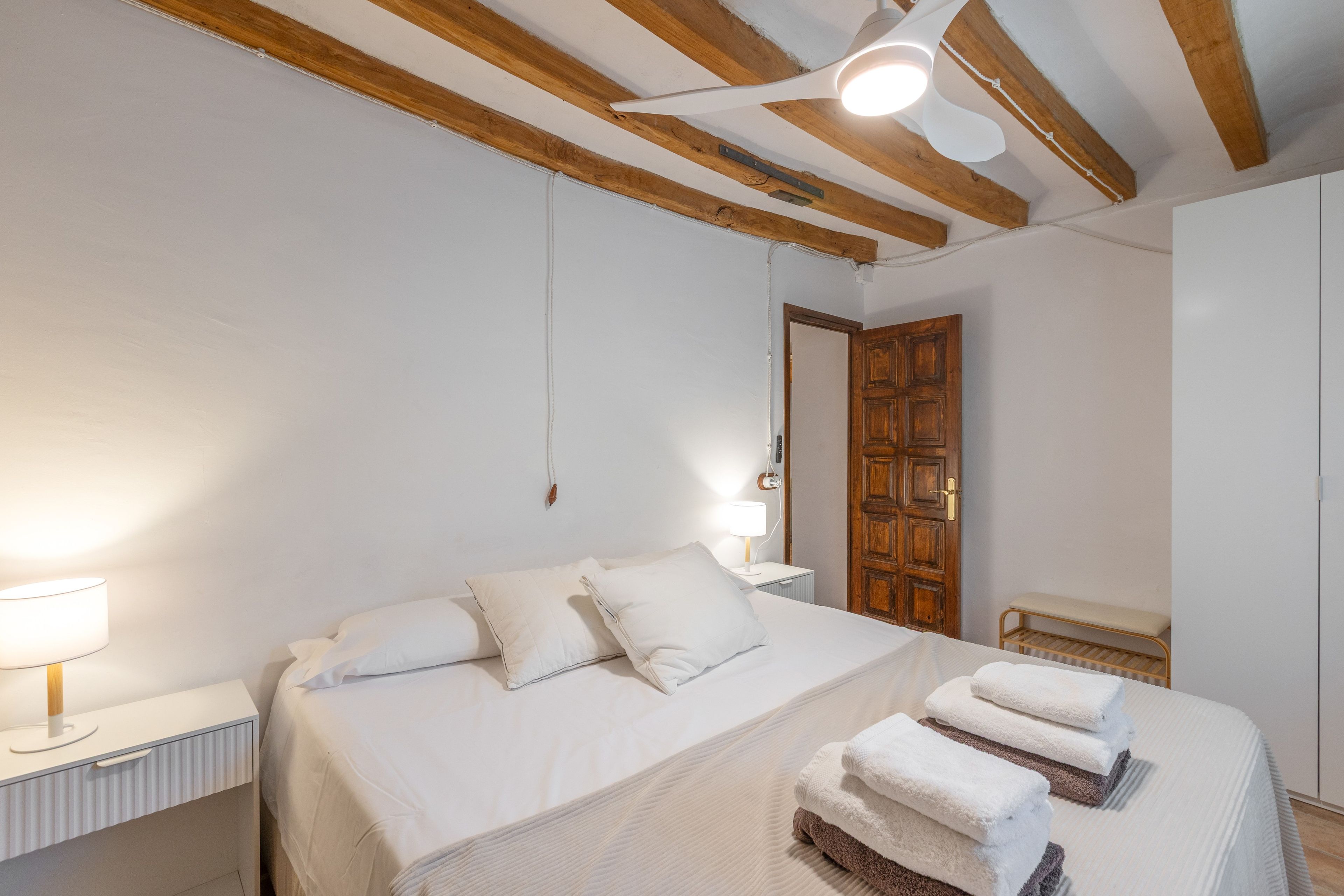Un dormitorio con cama, lámparas de noche, una puerta de madera y un ventilador de techo.