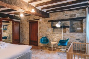 Una habitación rústica con pared de piedra, vigas de madera, una cama, un escritorio y dos sillas.