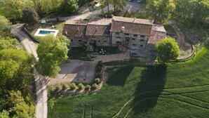 A stone building with a tiled roof, surrounded by lush greenery and a swimming pool.