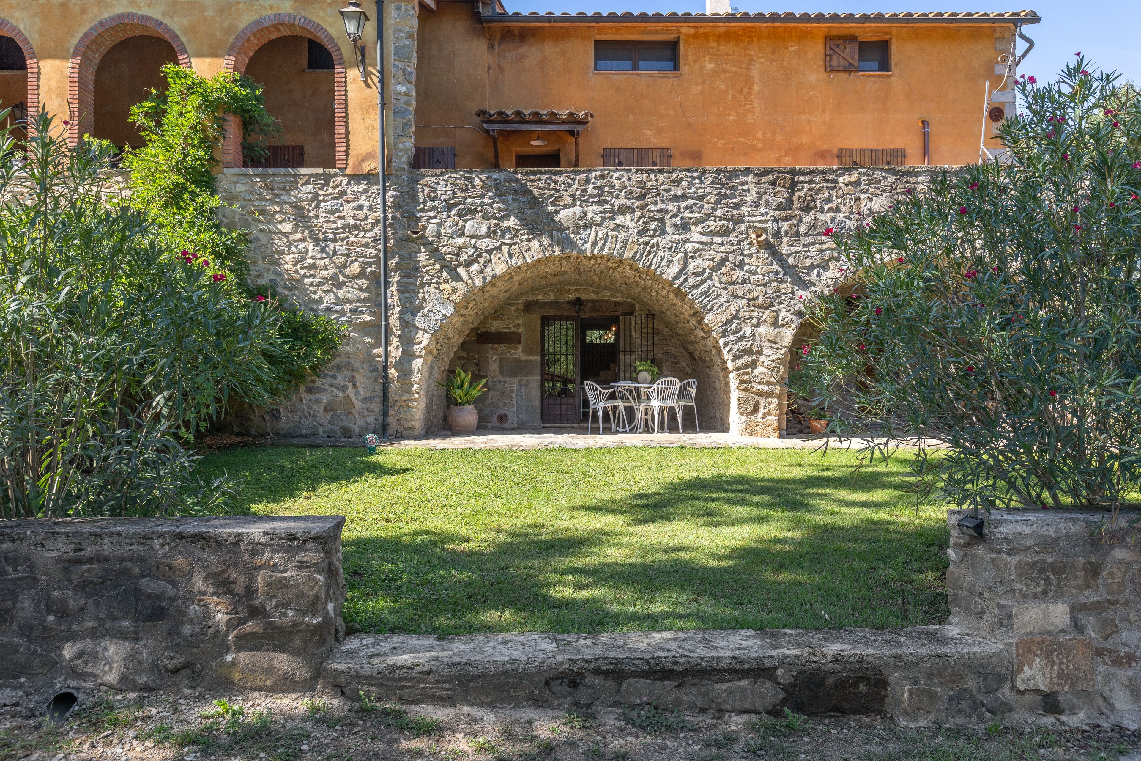 A stone building with a courtyard, a dining area with chairs, and a small garden.