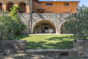 A stone building with a courtyard, a dining area with chairs, and a small garden. - Holiday Home 'Can Blanc - 11 Persones' with Mountain View, Shared Pool and Wi-Fi (Montagut)