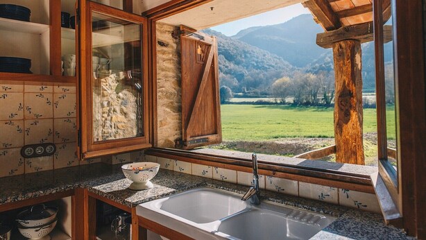 A kitchen with a large window, granite countertops, and a view of a green landscape.