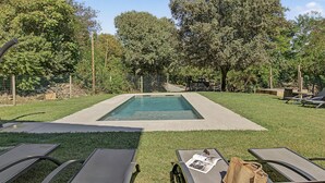 A rectangular swimming pool with a tiled deck, surrounded by a grassy area and trees.