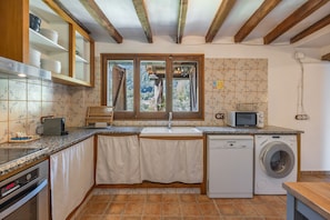 Cocina compacta con lavadora integrada, microondas y ventana con vistas a zonas verdes.