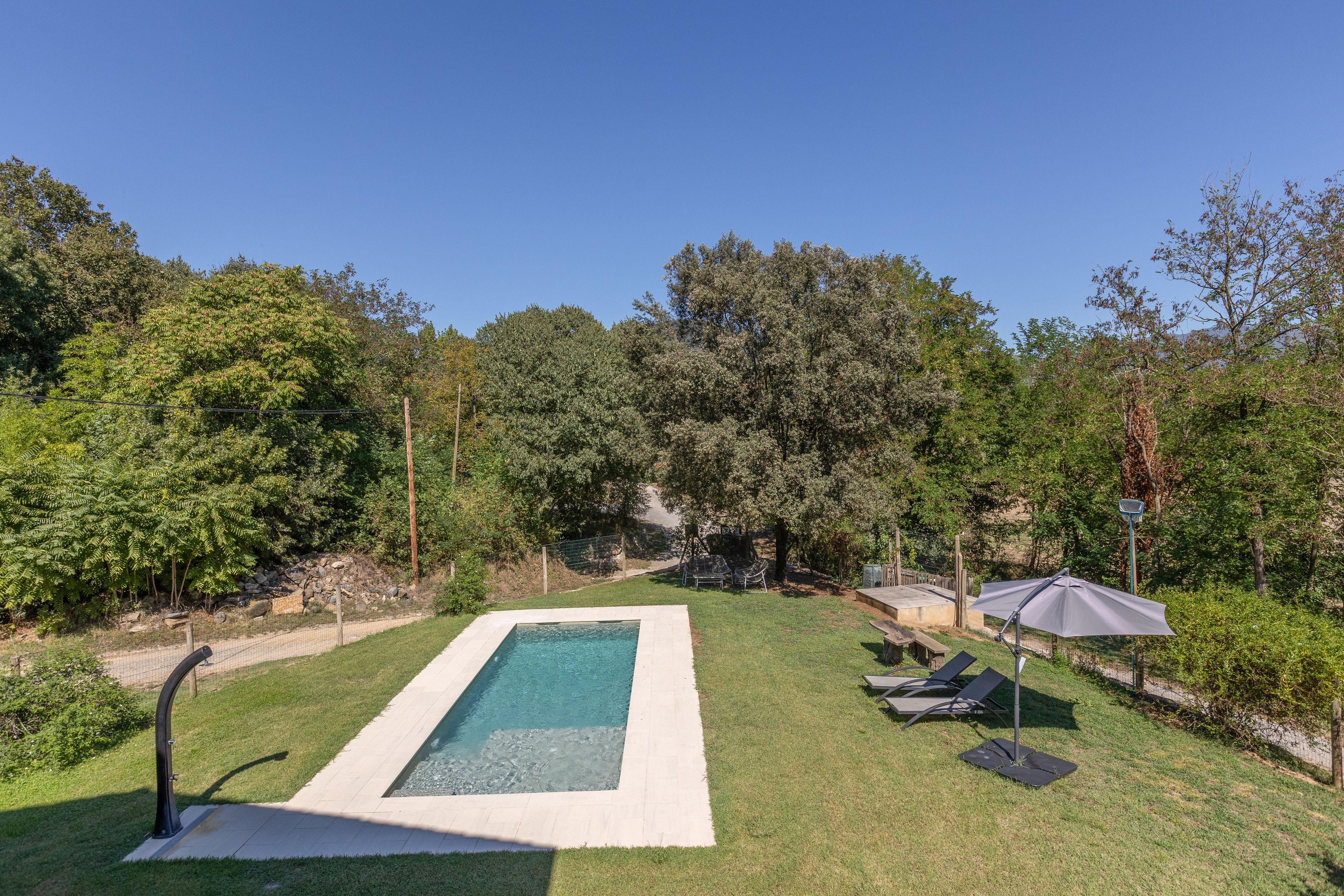 Una piscina rectangular con solárium empedrado, rodeada de césped y árboles.