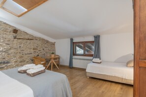 Ein Zimmer mit Steinwand, Holzboden, einem Bett, einem Tisch mit Stühlen und einem Fenster mit Vorhängen.
