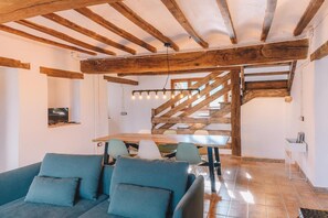 Un interior moderno con vigas de madera a la vista, un comedor con mesa y sillas de madera, y un sofá con cojines.