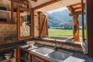 Una cocina con un ventanal grande, encimeras de granito y vistas a un campo verde y montañas.