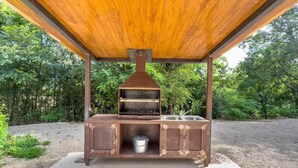 Un barbecue extérieur en bois, doté d’une cheminée, d’un évier et d’un récipient en métal.