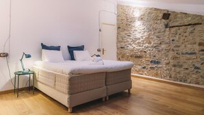 Une chambre à coucher avec un lit, une table de chevet, une lampe, un mur en pierre et un plancher en bois.