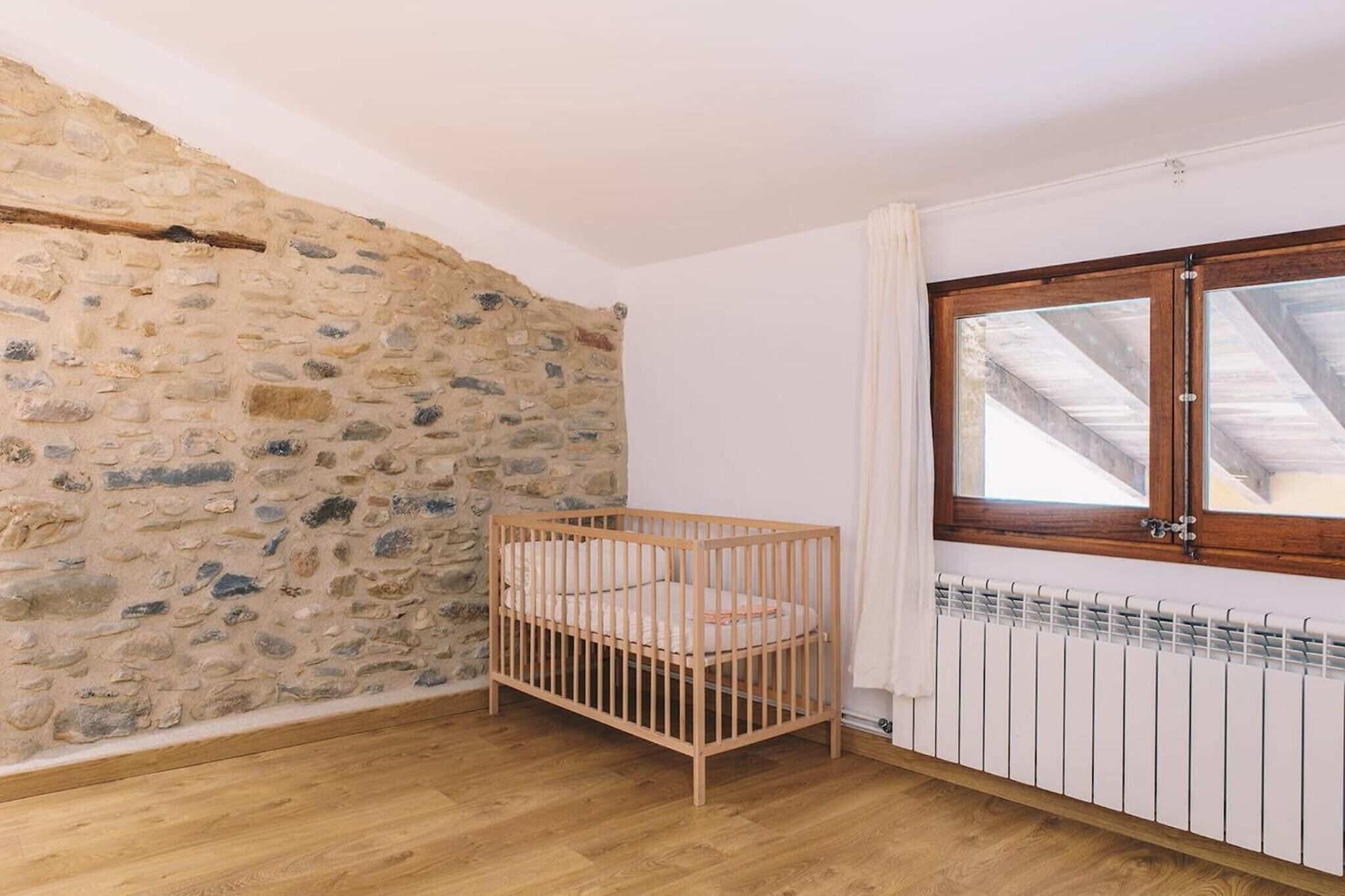 A room with a stone wall, a wooden crib, a window with a wooden frame, and a white radiator.