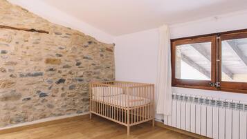A room with a stone wall, a wooden crib, a window with a wooden frame, and a white radiator.