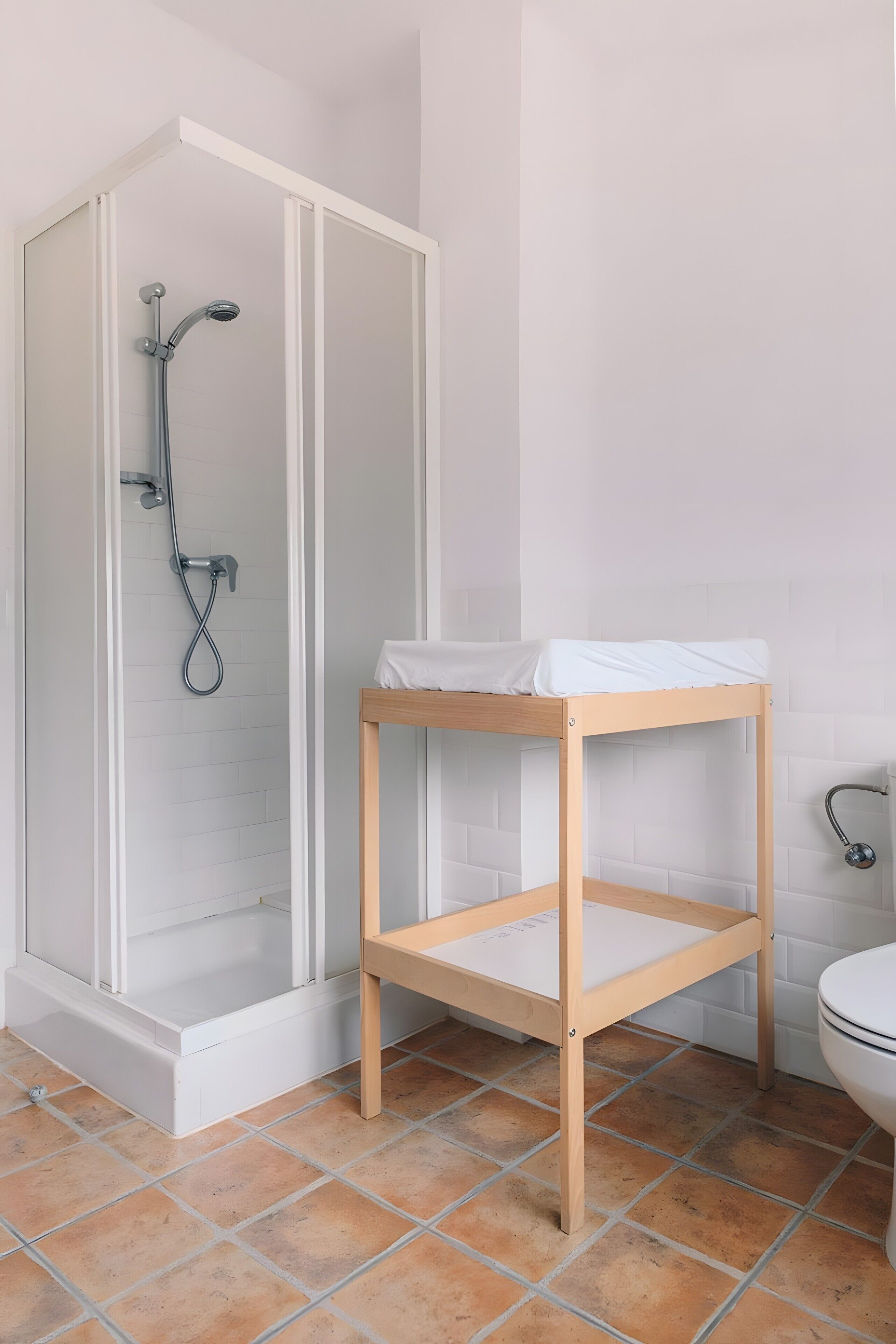 Un baño con cabina de ducha, estante de madera y un inodoro.