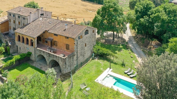 A stone building with a courtyard, a swimming pool, and surrounding greenery.