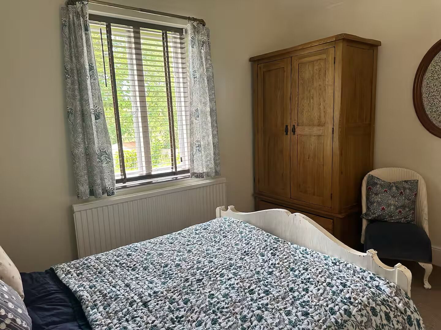 Una camera da letto con un letto, un armadio in legno, una finestra con tende e una sedia.