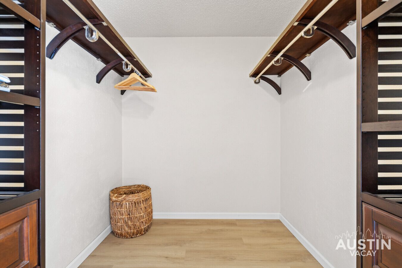 Habitación de esquina con piso de madera, una cesta tejida y un perchero de madera en una barra de metal.