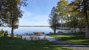 En campingplats vid en sjö med en brygga, ett takförsett område för picknick och en liten stuga.