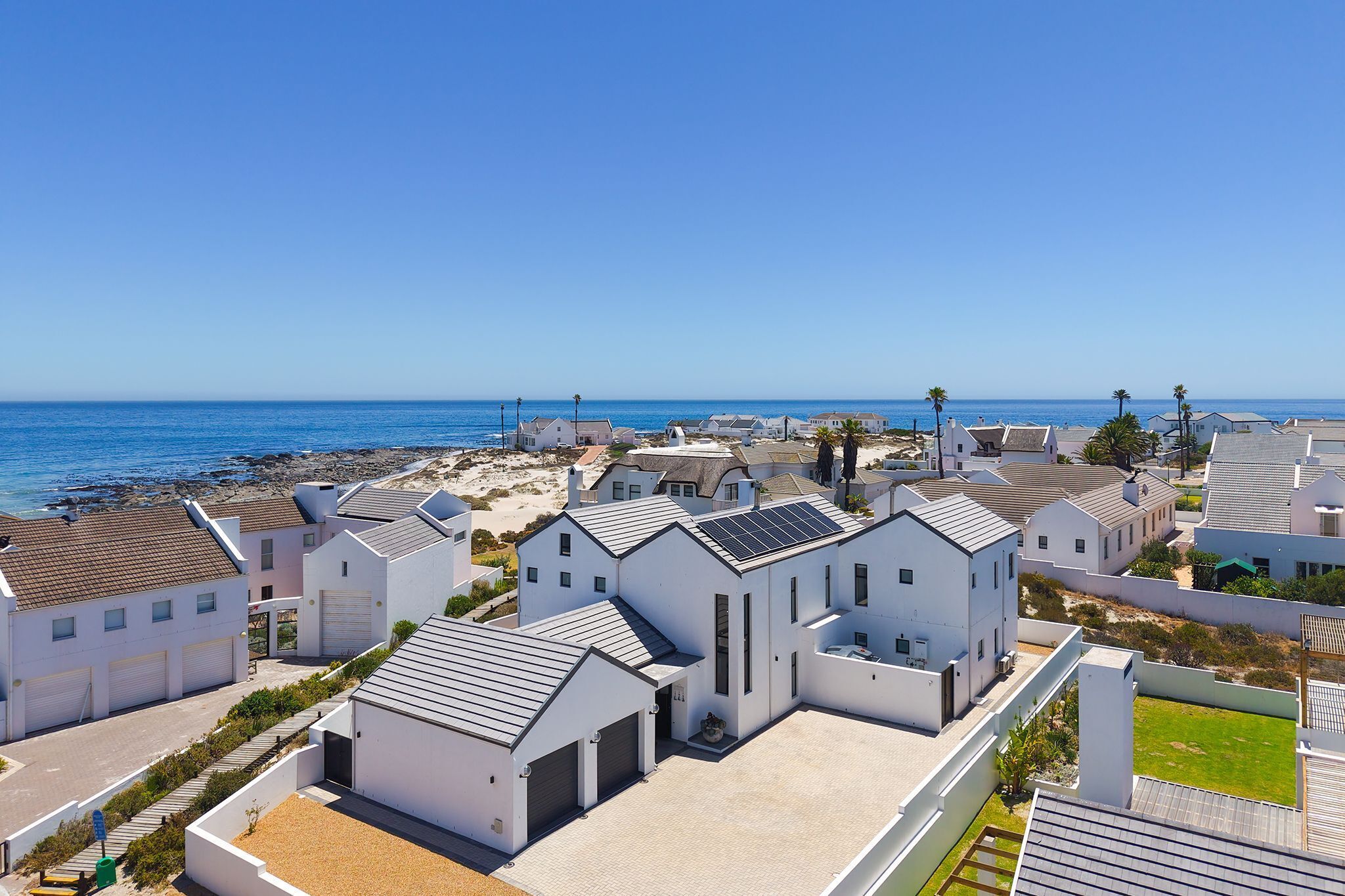 A coastal residential area with white houses, a beach, and a clear blue sky.