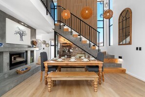 A dining area with a wooden table set for four, a fireplace, and a staircase with a wooden railing.