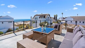 Una terraza en la azotea con muebles de mimbre, una mesa con cubierta de vidrio y vistas a la playa y al océano.