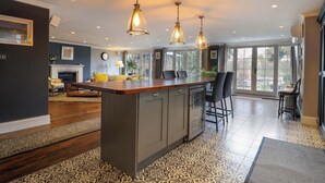 A modern kitchen with a central island, pendant lighting, and a view to the outside. - River Haven - River Thames Frontage House (Thames Ditton)
