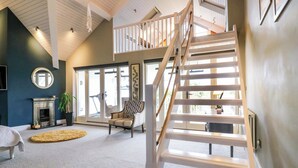 A spacious living room with a high ceiling, a staircase, a fireplace, and a large window. - River Haven - River Thames Frontage House (Thames Ditton)
