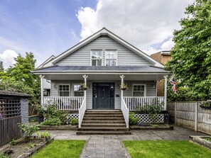 A two-story house with a front porch, a black front door, and a small garden area with a wooden fence. - River Haven - River Thames Frontage House (Thames Ditton)