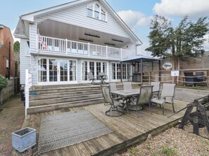 A two-story house with a covered patio area, outdoor seating, and a garden sign. - River Haven - River Thames Frontage House (Thames Ditton)