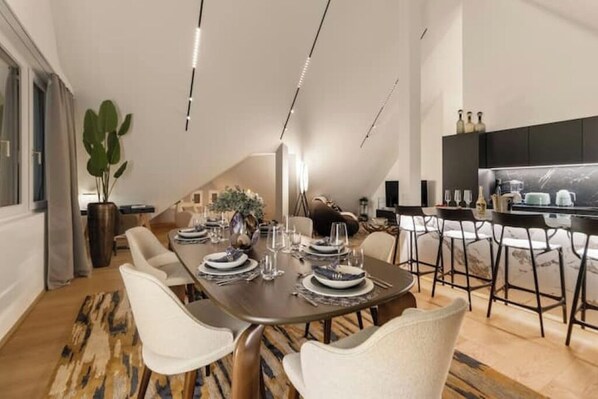 A modern dining area with a long table set for six, surrounded by white chairs. - Bahnhofstrasse Designer Penthouse Private Rooftop (Zürich)