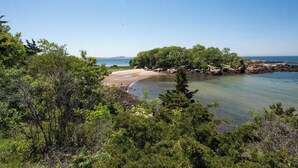 Et kystlandskab med sandstrand, klippeudspring og frodig grøn vegetation.