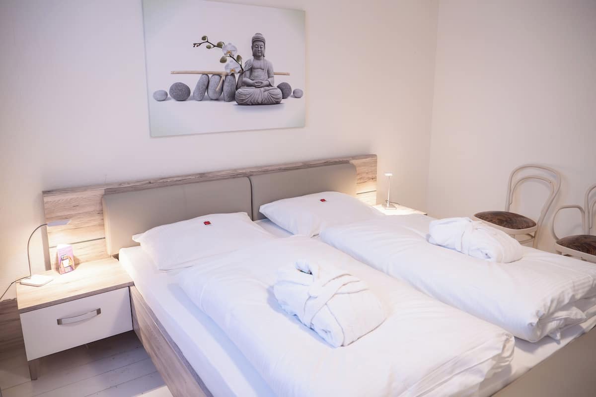 Een hotelkamer met twee bedden, een nachtkastje, een stoel en een aan de muur hangend kunstwerk van een Boeddhabeeld.