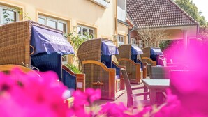 Outdoor wicker furniture with blue umbrellas, a building with a tiled roof, and a brick pathway. - Hekmat Apartments Husum Nordsee (Husum)
