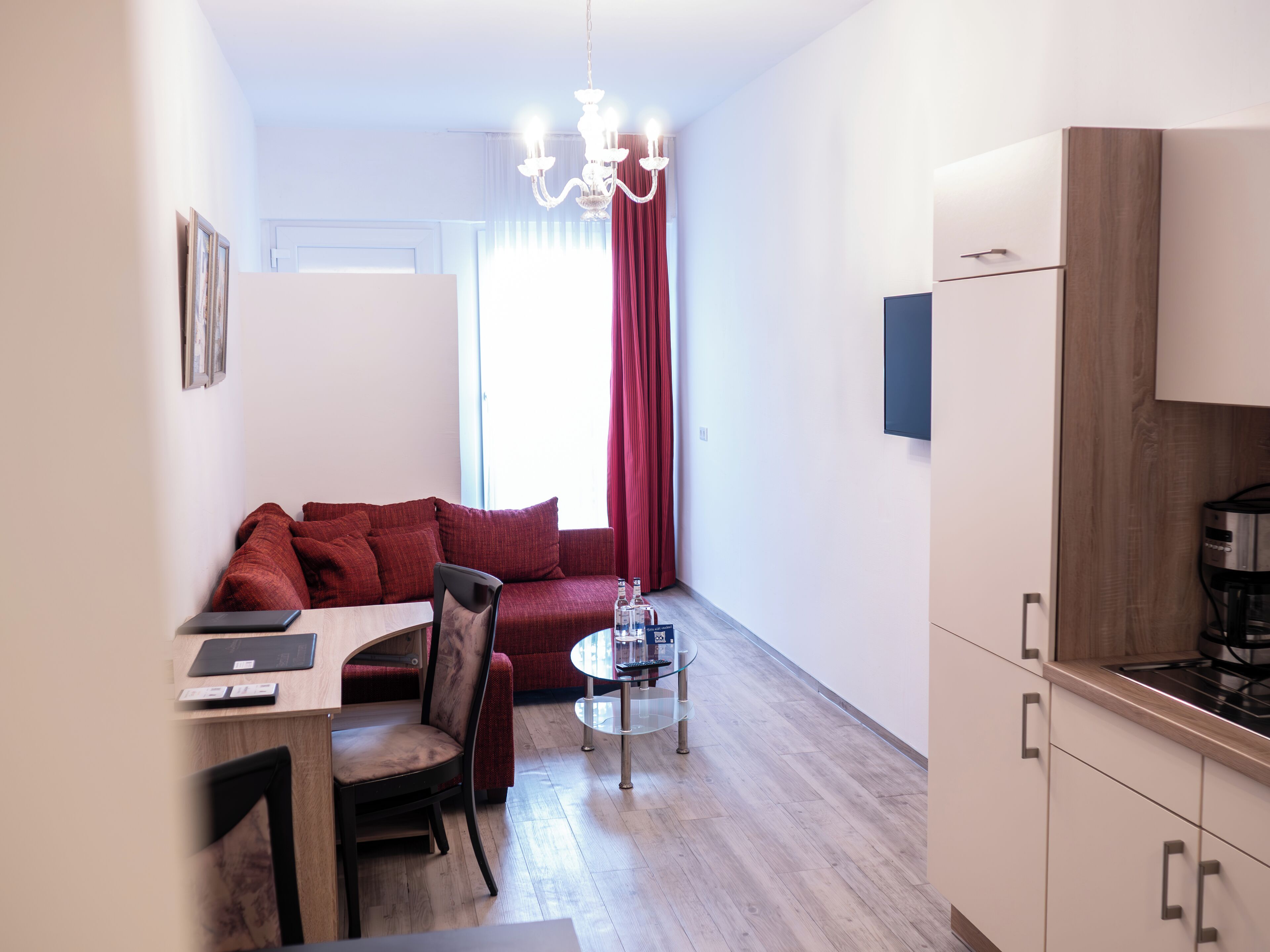 Un espace de vie compact comprenant un coin cuisine, un espace repas avec une table et des chaises, un canapé et un lustre.