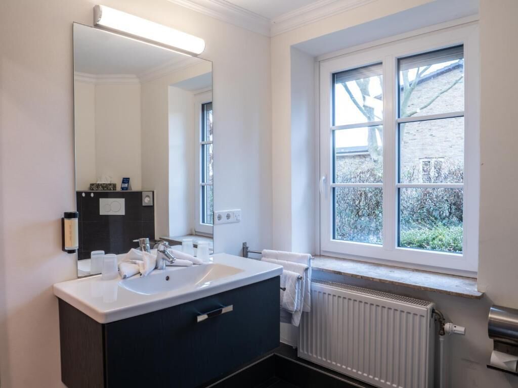 A modern bathroom with a white sink, dark vanity, and a large mirror. There is a window with a view of greenery outside.
