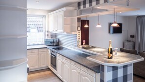 A modern kitchen with white cabinetry, a granite countertop, and pendant lighting. - Hekmat Apartments Husum Nordsee (Husum)