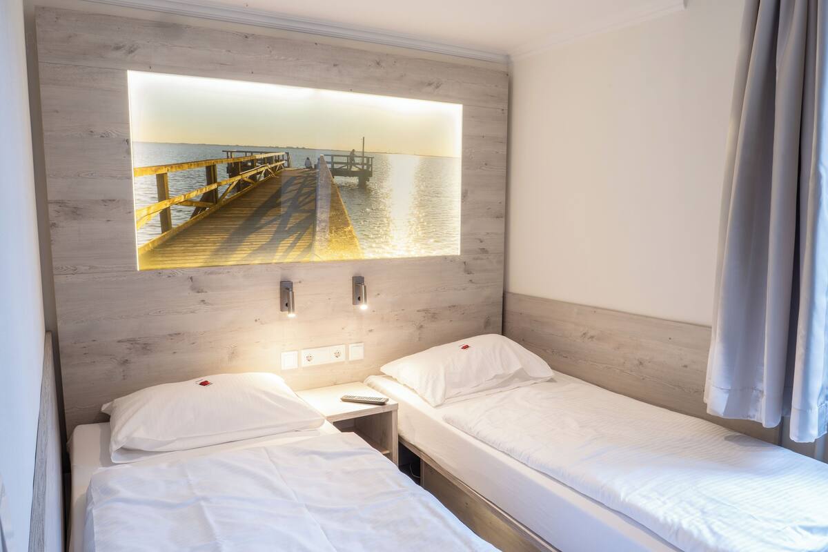 Een hotelkamer met twee enkele bedden, een houten hoofdbord, een nachtkastje en een tv aan de muur waarop een uitzicht op een haven en water te zien is.