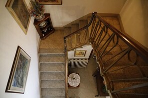 Un escalier avec une rampe en bois, un radiateur et une petite table ronde recouverte d’une nappe en dentelle.