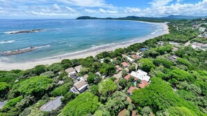 Ett flygbildsbild av ett kustområde med en strand, tät vegetation och bostadshus.