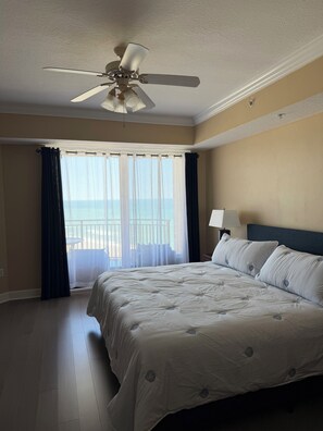 Ein Hotelzimmer mit einem Bett, einem Deckenventilator, einem Fenster mit Vorhängen und Blick auf den Strand.