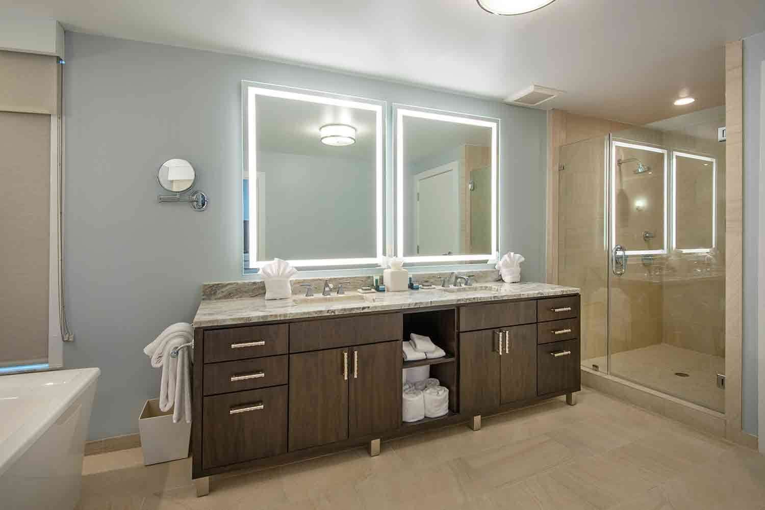 A modern bathroom with a double vanity, large mirrors, a walk-in shower, and a toilet.