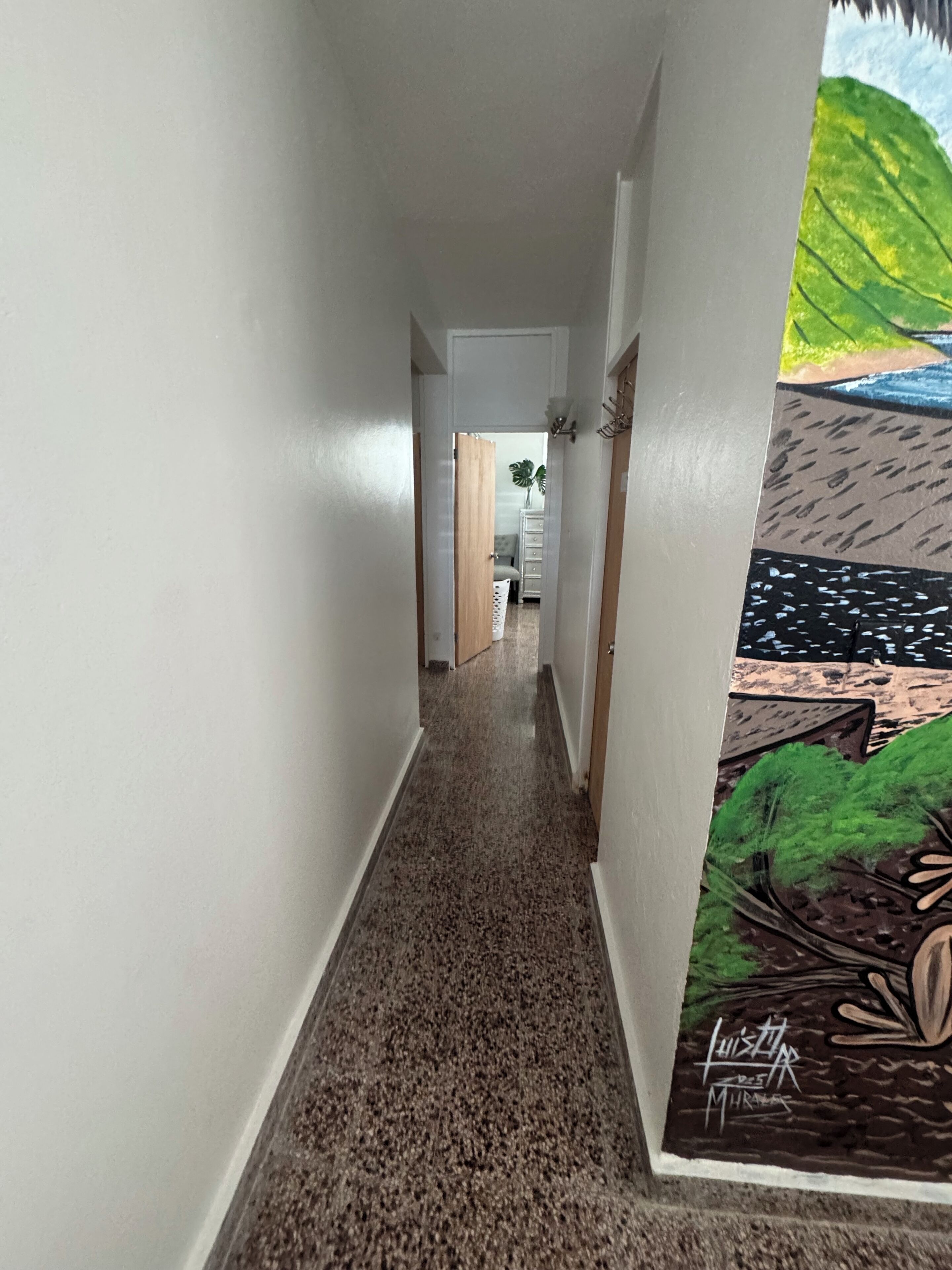 Ein Flur mit einem gemusterten Boden, weißen Wänden und einer Tür zu einem Zimmer mit einer Pflanze.
