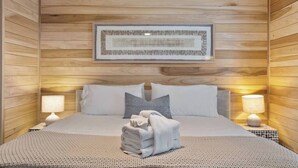 Una cama bien hecha con una toalla doblada, dos lámparas de noche y una obra de arte enmarcada en la pared.