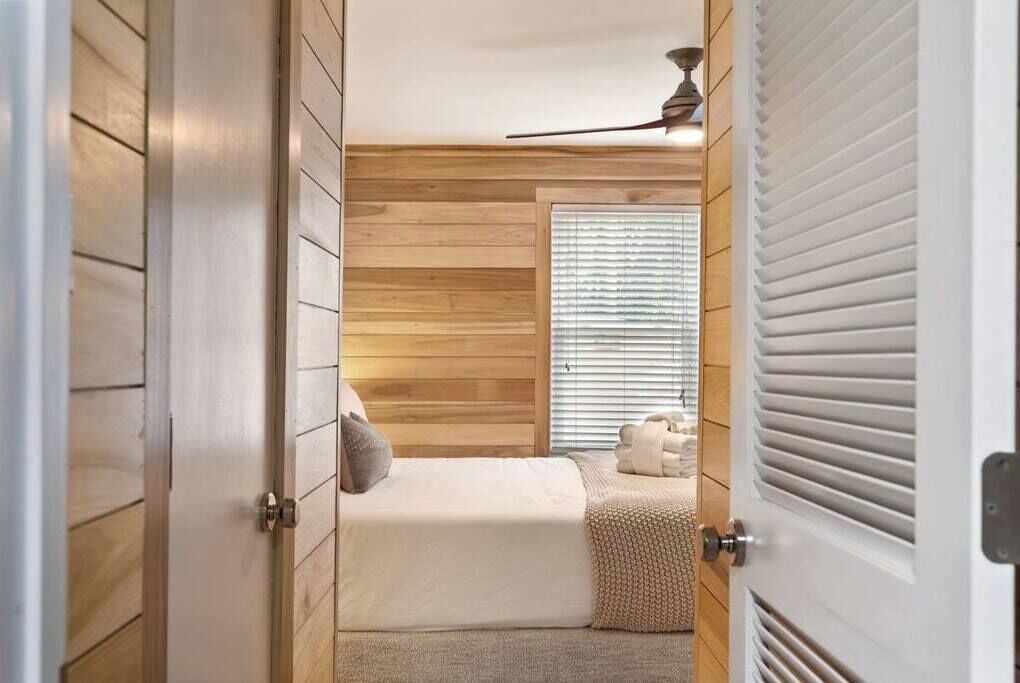 A bedroom with a bed, a window with blinds, a ceiling fan, and a door.