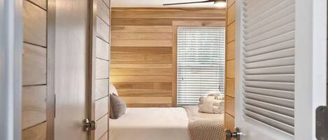 A bedroom with a bed, a window with blinds, a ceiling fan, and a door.
