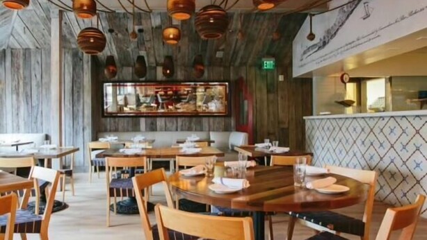 Un restaurante con mesas y sillas de madera, lámparas colgantes y una pared con estampado.
