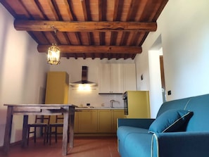 A kitchen with wooden beams, a dining table, chairs, a yellow cabinet, and a blue sofa.