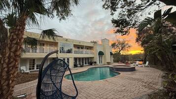 A pool area with a lounge chair, a two-story building with balconies, and a sunset in the background.